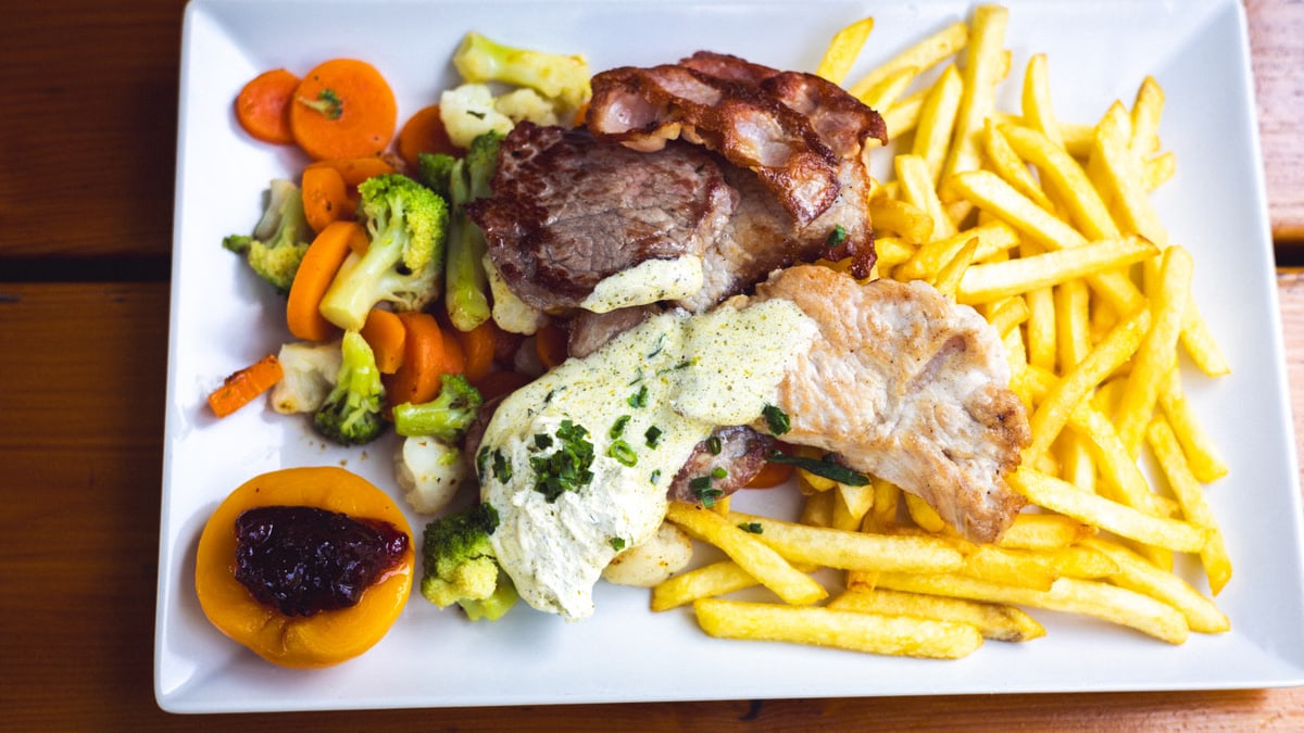 Appetizing meal of grilled meat, fresh vegetables, and crispy fries on a plate.